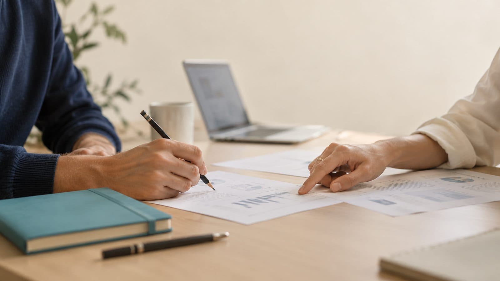 Deux personnes annotent des documents autour d'un ordinateur portable